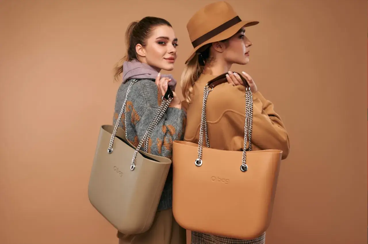 Dwie kobiety prezentują modne torebki na lato. Jedna w beżowym swetrze, druga w brązowym kapeluszu.