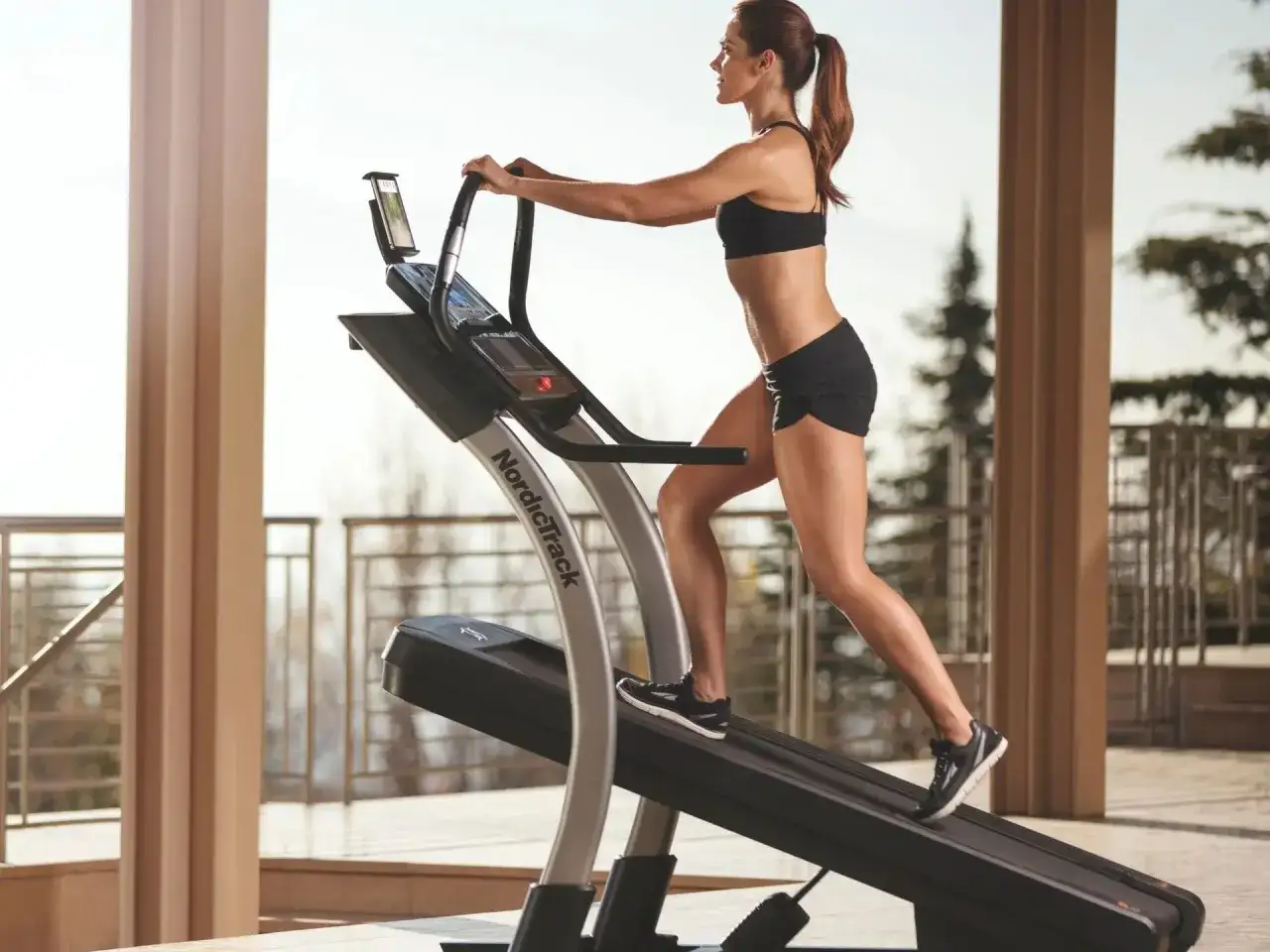 Kobieta ćwiczy na bieżni NordicTrack na tarasie z widokiem na drzewa.