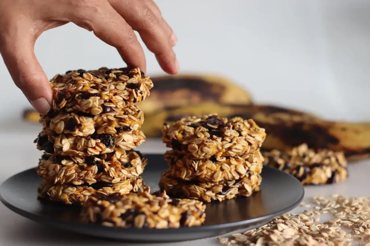 Ręka sięga po stos chrupiących ciasteczek owsianych z rodzynkami i suszonymi owocami.