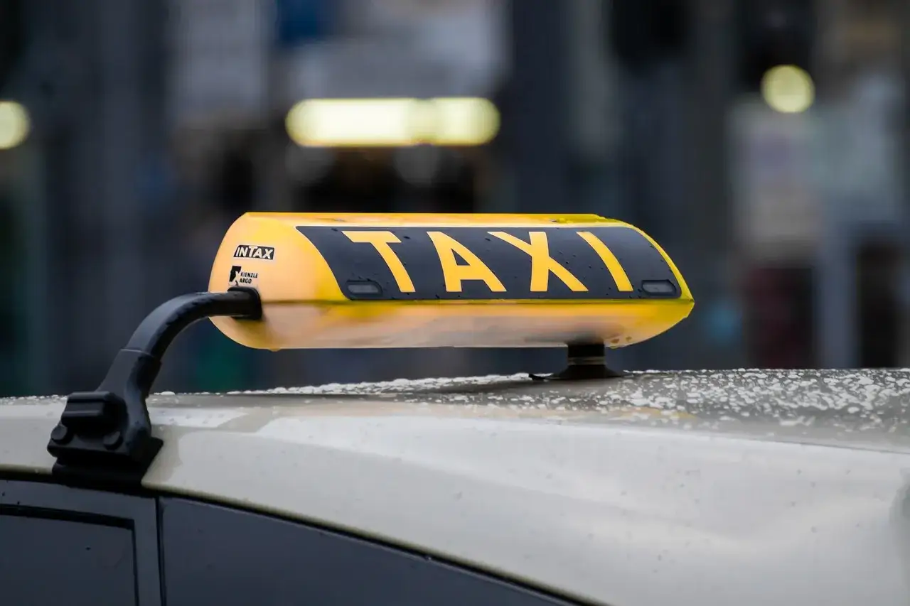 Żółty dachowy znak TAXI na samochodzie, z widocznymi kroplami deszczu.