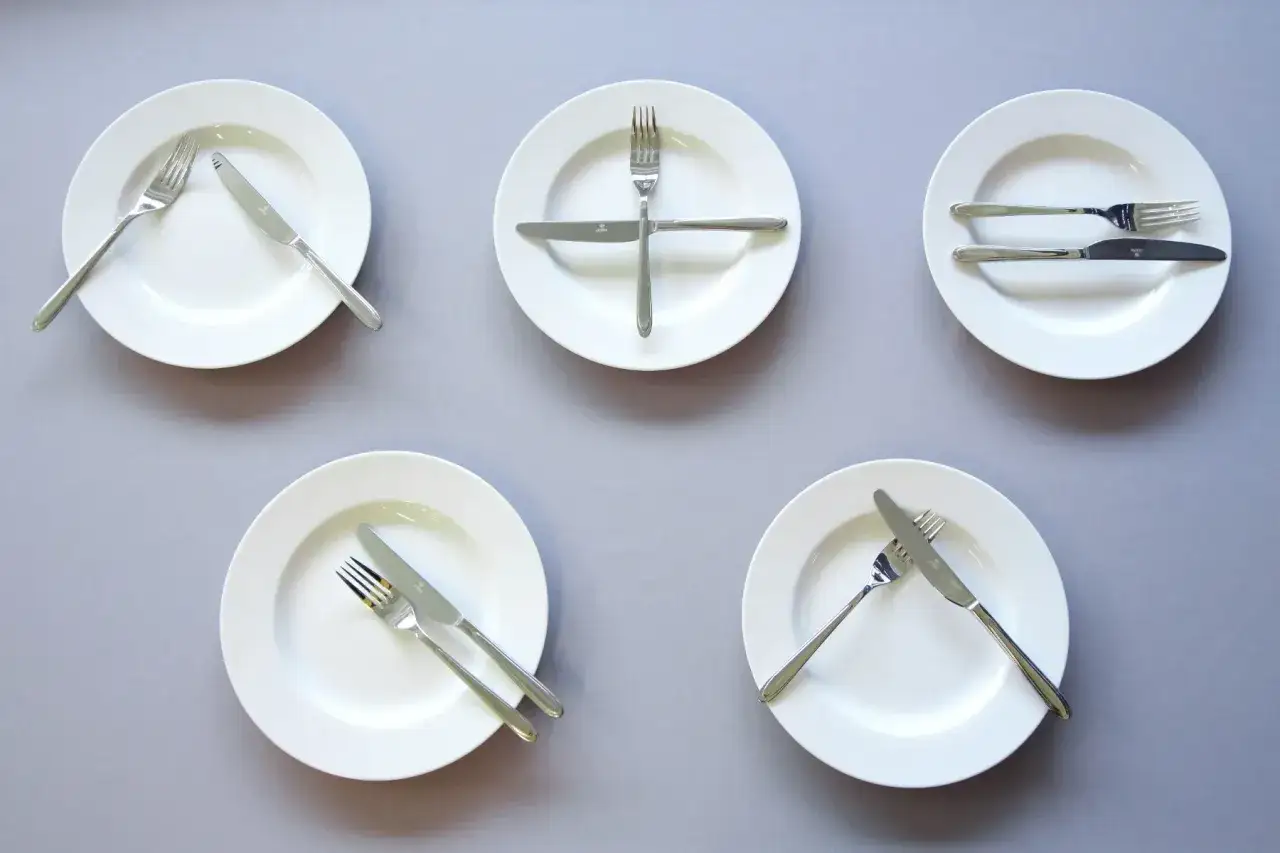Pięć talerzy z różnie ułożonymi sztućcami, wskazujących jak jesc catering.