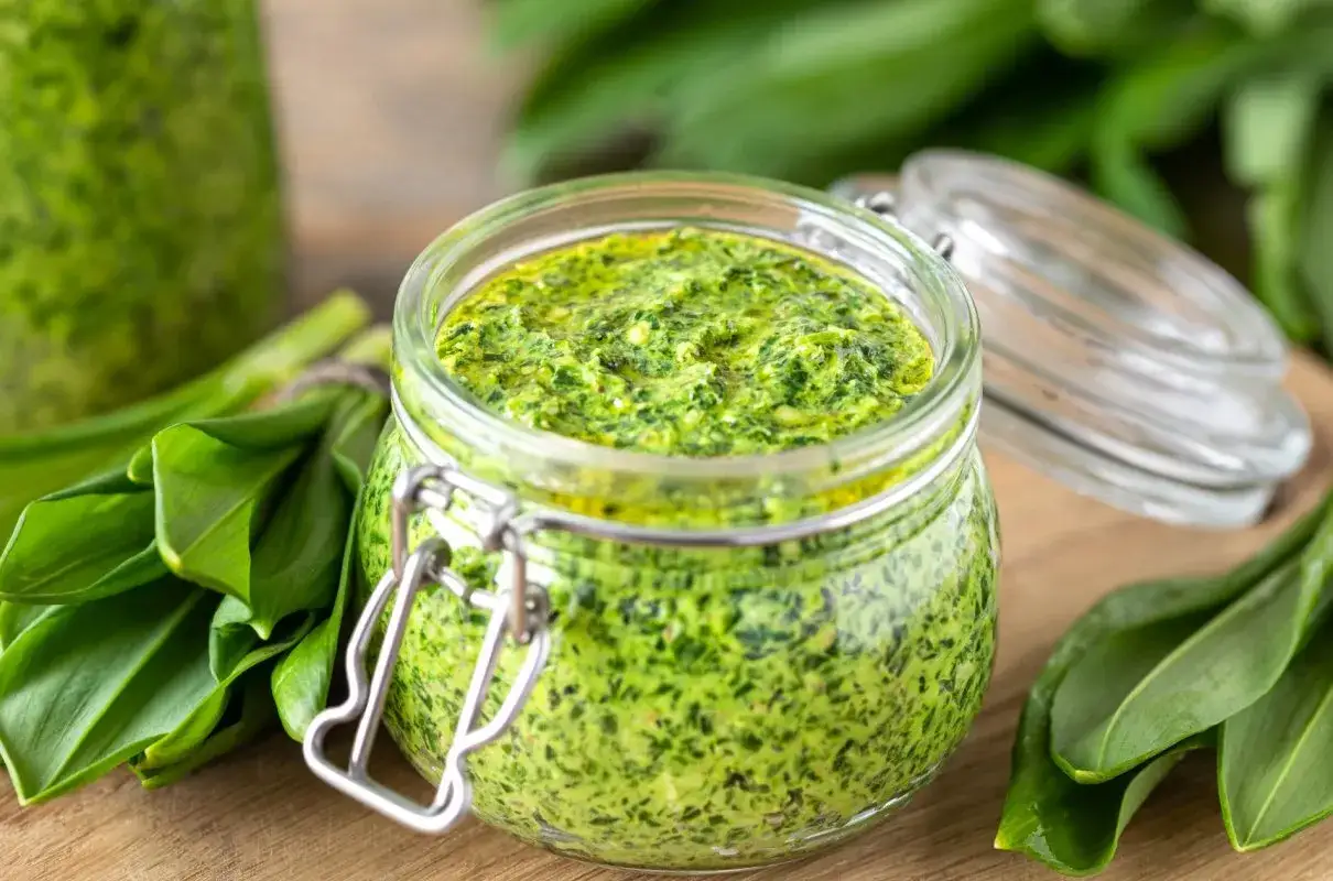 Słoik pełen aromatycznego pesto z czosnku niedźwiedziego, otoczony świeżymi liśćmi tej wiosennej rośliny.