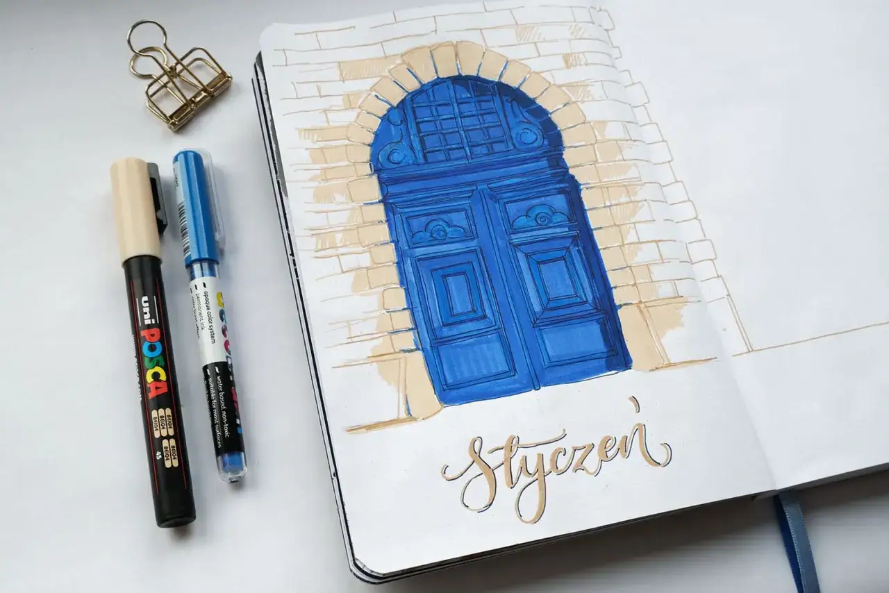 notes do rysowania: niebieskie drzwi pod łukiem z cegieł, obok pisaki i spinacz.