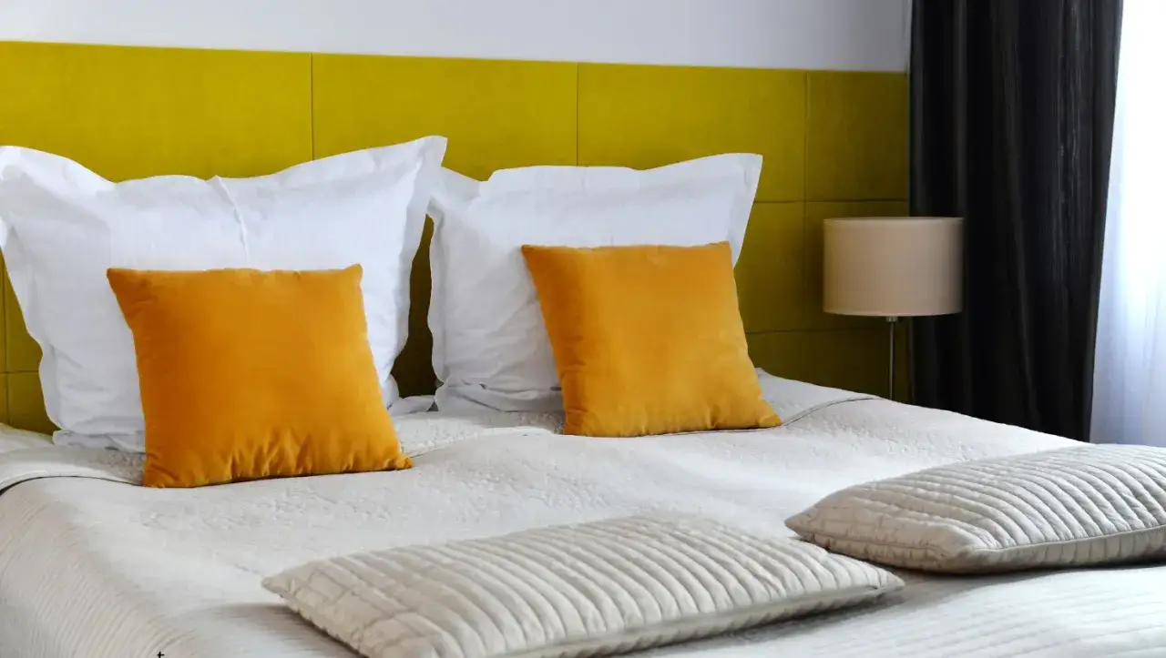 Łóżko z białymi i żółtymi poduszkami na tle żółtej ściany.