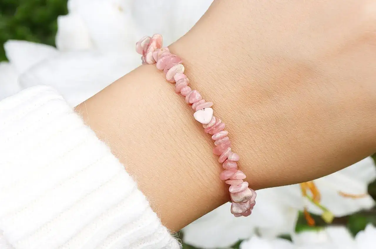 Różowa bransoletka z kamieni na nadgarstku, z serduszkiem pośrodku.