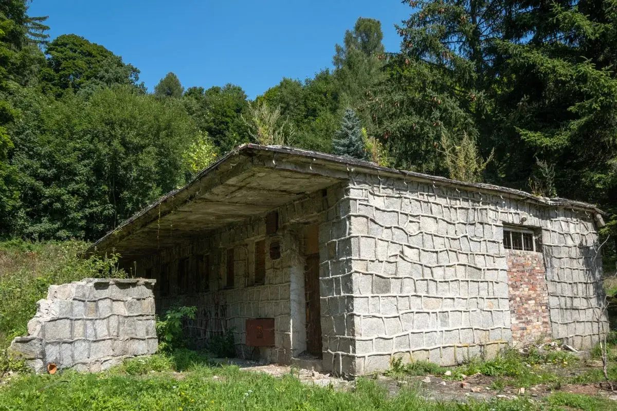 Kamienna bacówka pod Trójgarbem, otoczona zielenią, zniszczona przez czas.