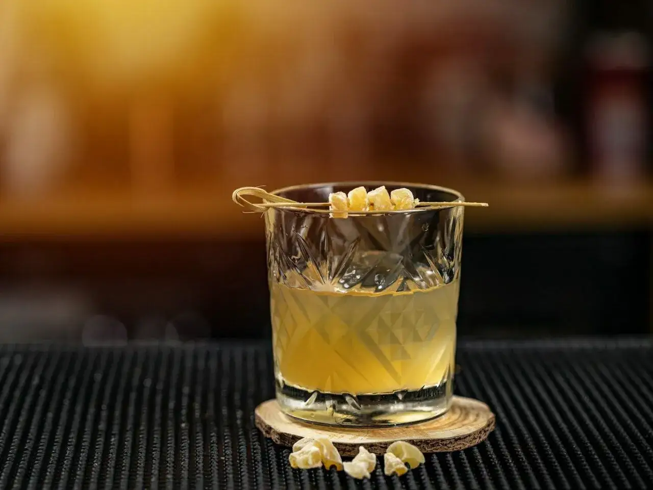 Orzeźwiający drink Ballantines z colą, ozdobiony kandyzowanym imbirem, na drewnianym podkładzie.