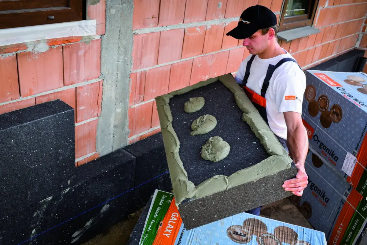Budowlaniec przygotowuje się do montażu, kiedy kołkować styropian. Klej na płycie izolacyjnej.