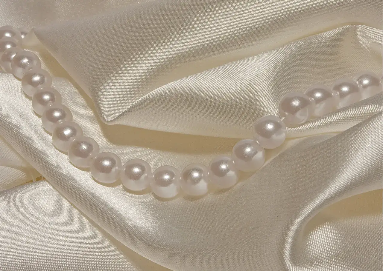 Perły na kremowym jedwabiu. Delikatne fałdy i połysk tkaniny pomogą Ci jak rozpoznać jedwab.