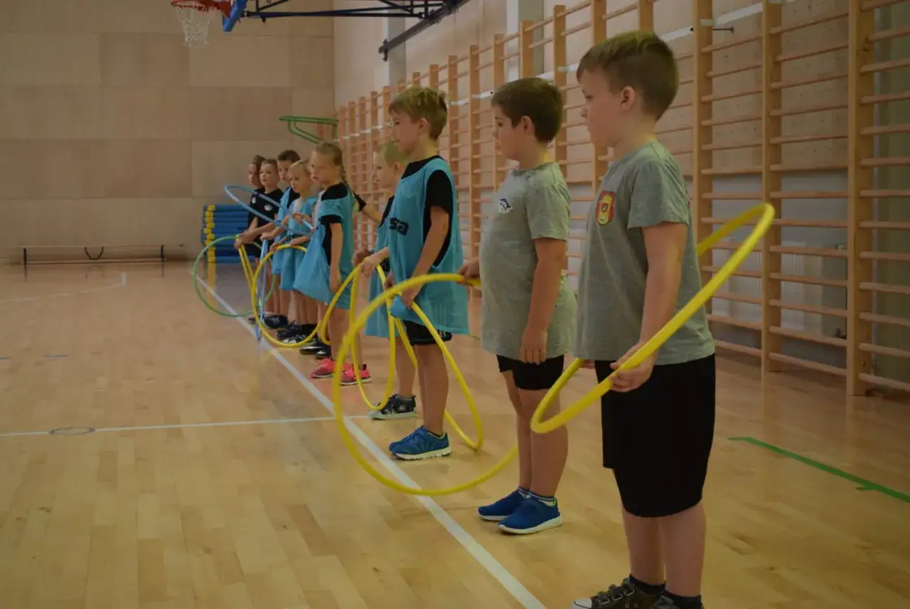 Dzieci z klas 1-3 na lekcji WF ćwiczą z hula-hop. Radosne gry i zabawy sportowe.