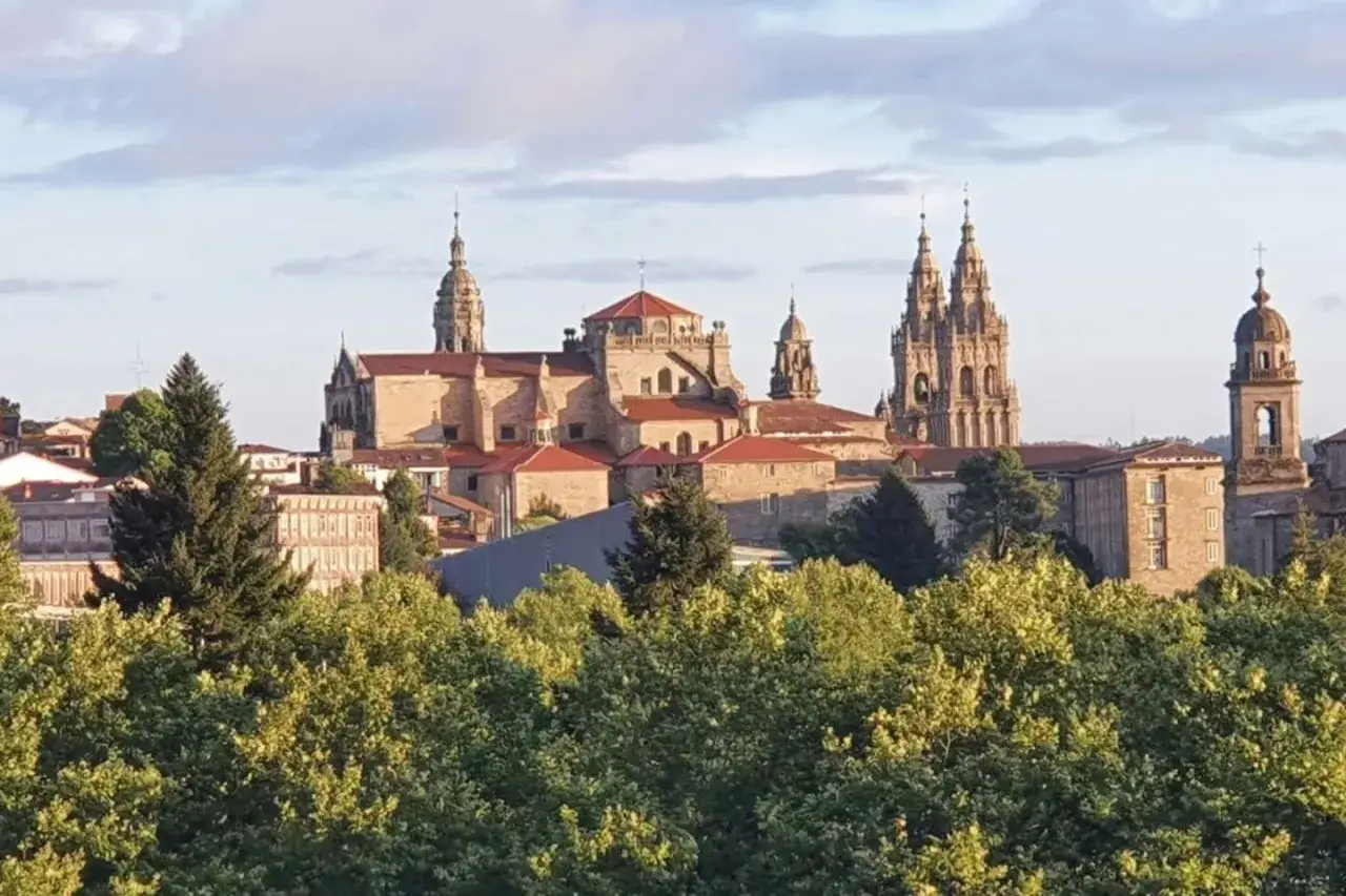 Majestatyczna katedra w Santiago de Compostela, cel pielgrzymek, wyłania się zza zieleni drzew.