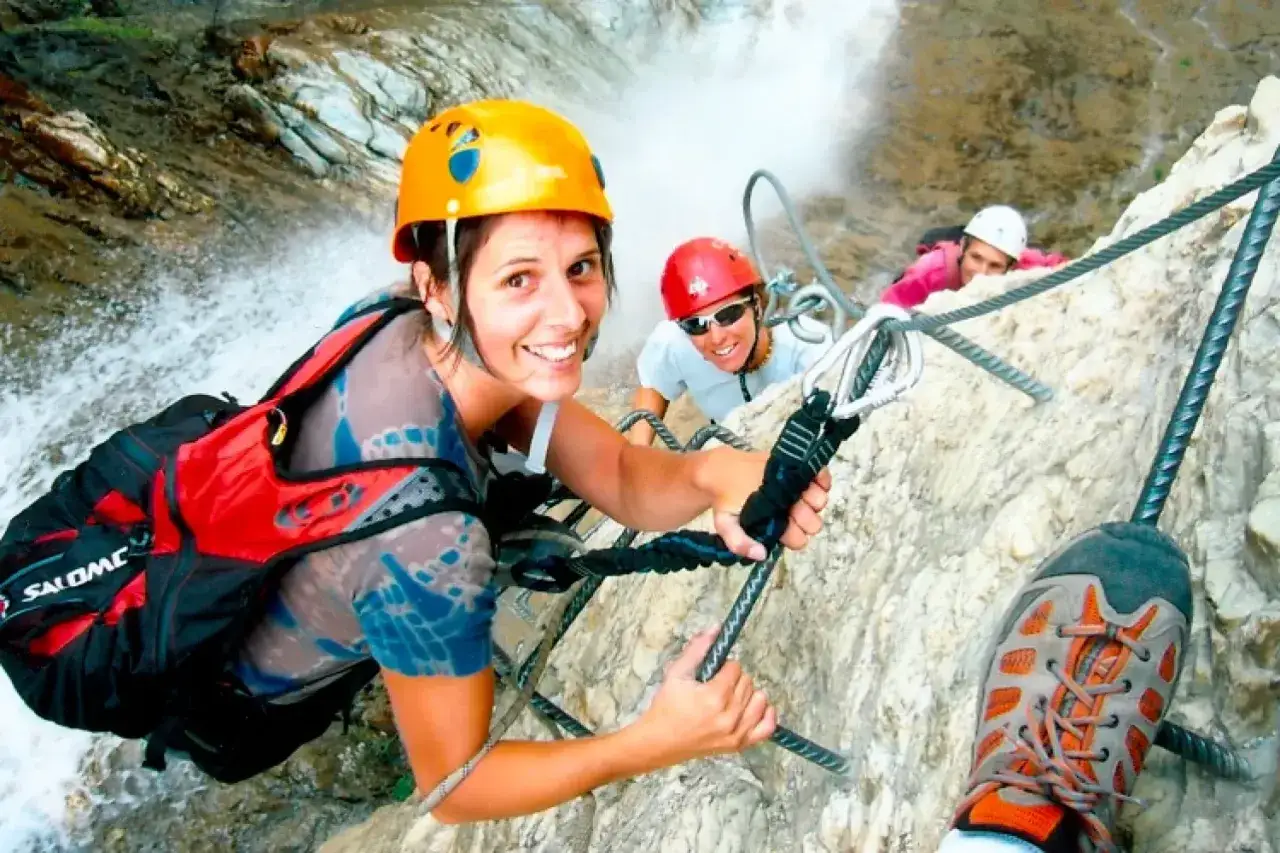 Kobieta w kasku i kamizelce asekuracyjnej na via ferracie, trzymająca linę.