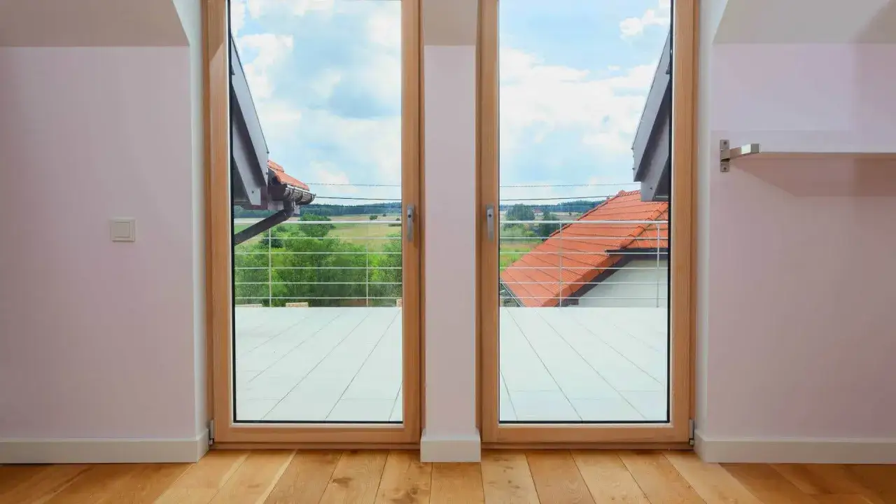 Drewniane okno balkonowe z widokiem na zielone pola i dachy. Zastanawiasz się, ile kosztuje okno balkonowe?