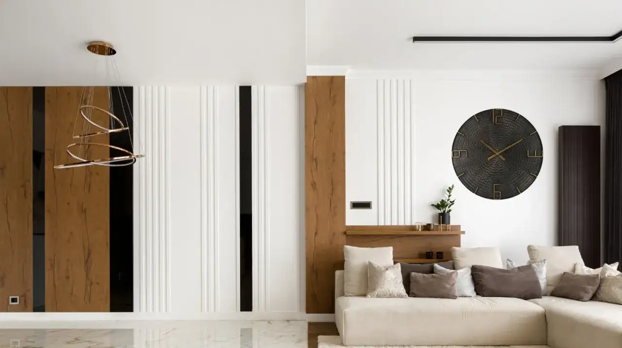 Nowoczesny zegar w salonie aranżacje. Duży, czarny zegar ścienny z metalicznymi wskazówkami nad beżową sofą.