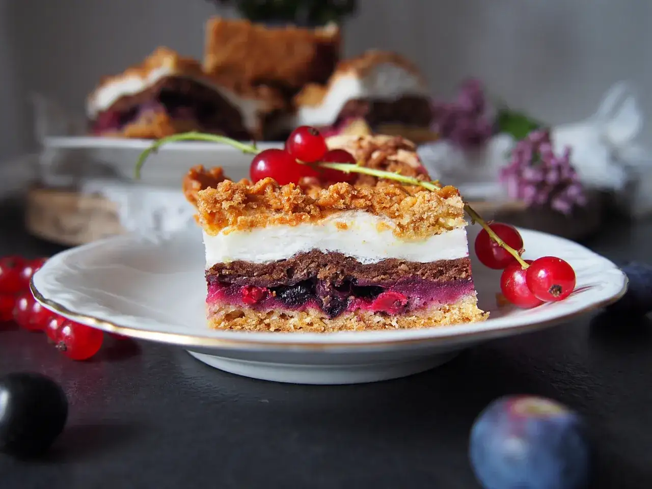 Pyszny kawałek ciasta pleśniak z dżemem porzeczkowym, ozdobiony świeżymi porzeczkami. Idealny na deser.