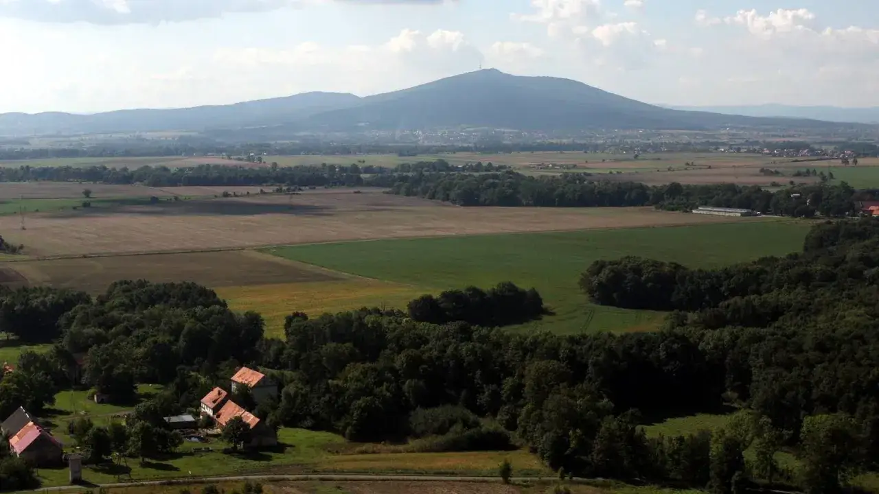 Widok na górzystą okolicę obok Wrocławia z polami, lasami i kilkoma domami.