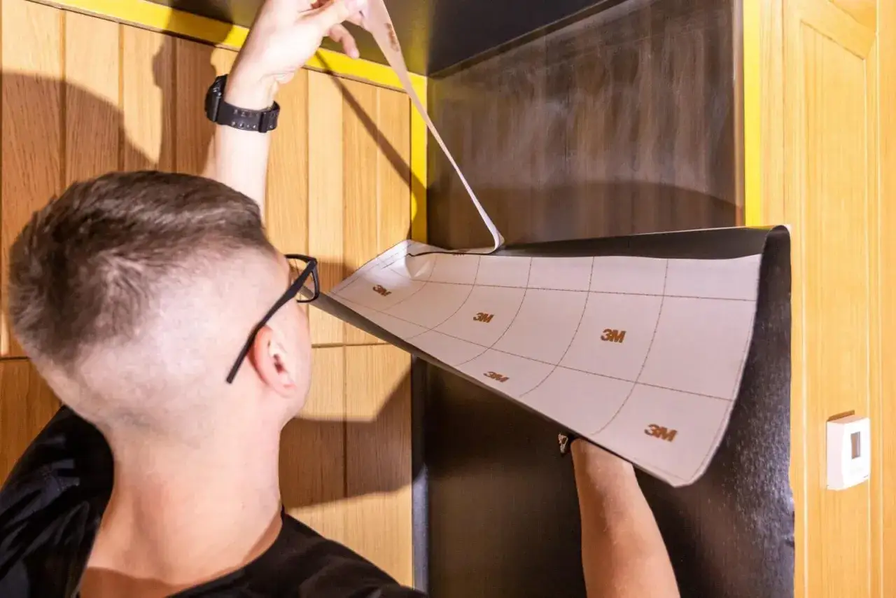 Mężczyzna okleja drzwi okleiną samoprzylepną. Pokazuje to, jak okleić drzwi okleiną samoprzylepną.