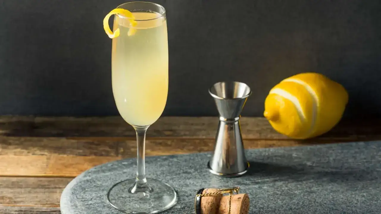 French 75 na ginie kontra French 75 na koniaku. Elegancki drink z cytrynową skórką, kieliszek, miarka barmańska, cytryna i korek od szampana.