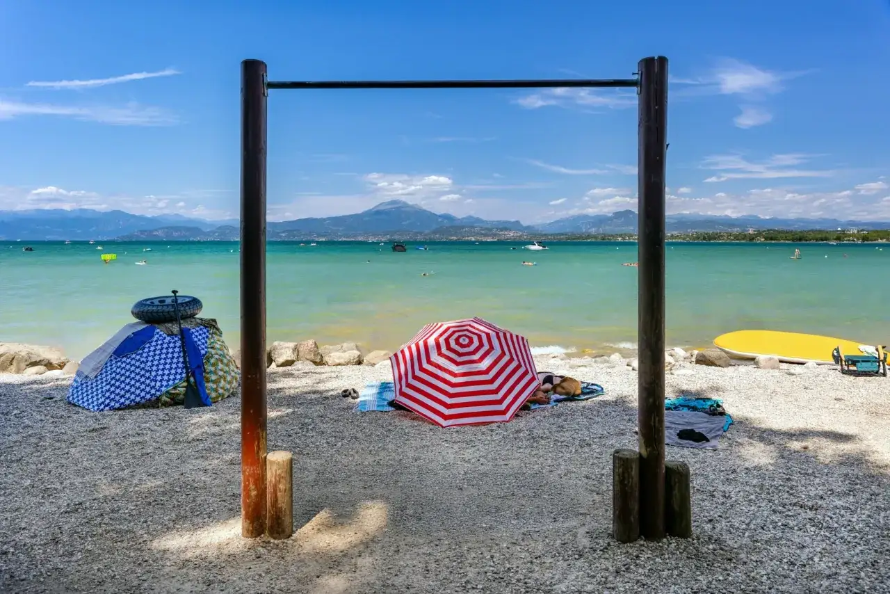 Słoneczne plaże nad jeziorem Garda, z parasolami, leżakami i wodnymi atrakcjami w tle.