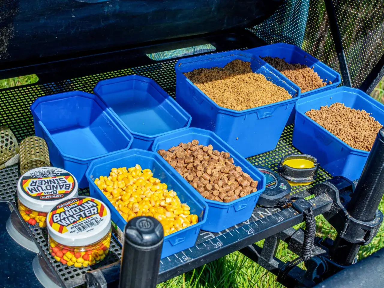 Gotowe pojemniki z zanętą feeder na zawody: kukurydza, pellety i sypka zanęta. Obok przynęty i akcesoria.