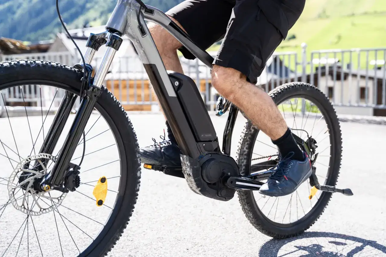 Mężczyzna pedałuje na rowerze elektrycznym, pokazując, jak działa rower elektryczny. Bateria i silnik są widoczne na ramie.