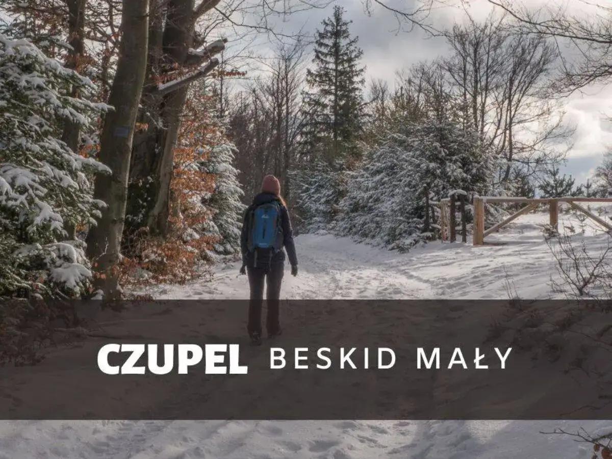 Kobieta w zimowej czapce i plecaku idzie zasypaną śniegiem trasą na Czupeł w Beskidzie Małym.