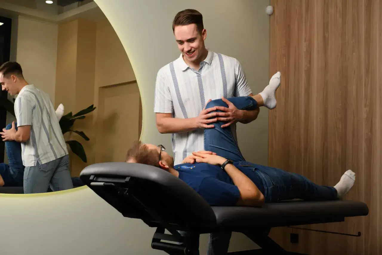 Fizjoterapeuta pomaga pacjentowi w ćwiczeniach nogi, co jest kluczowe w pytaniu: ile trwa rehabilitacja po artroskopii stawu skokowego.