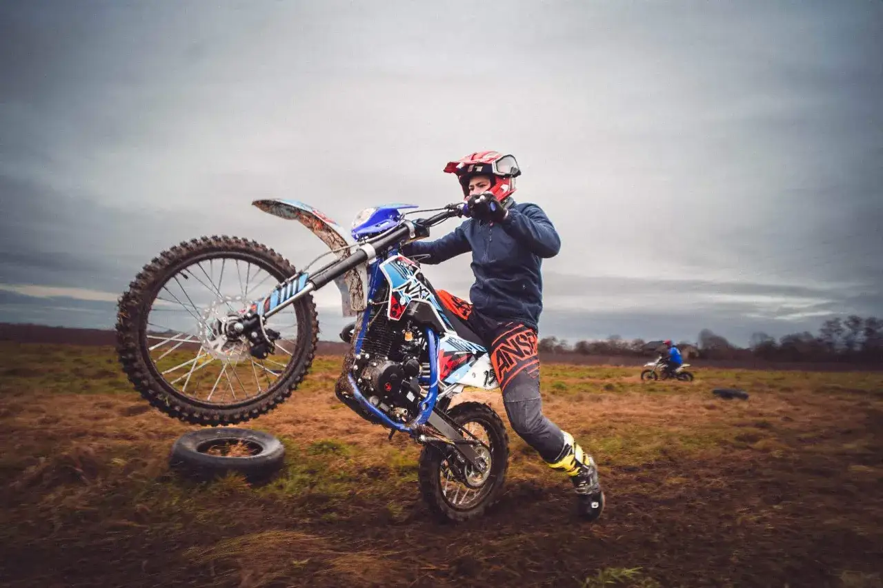 Młody motocyklista ćwiczy jazdę na jednym kole na błotnistym polu.