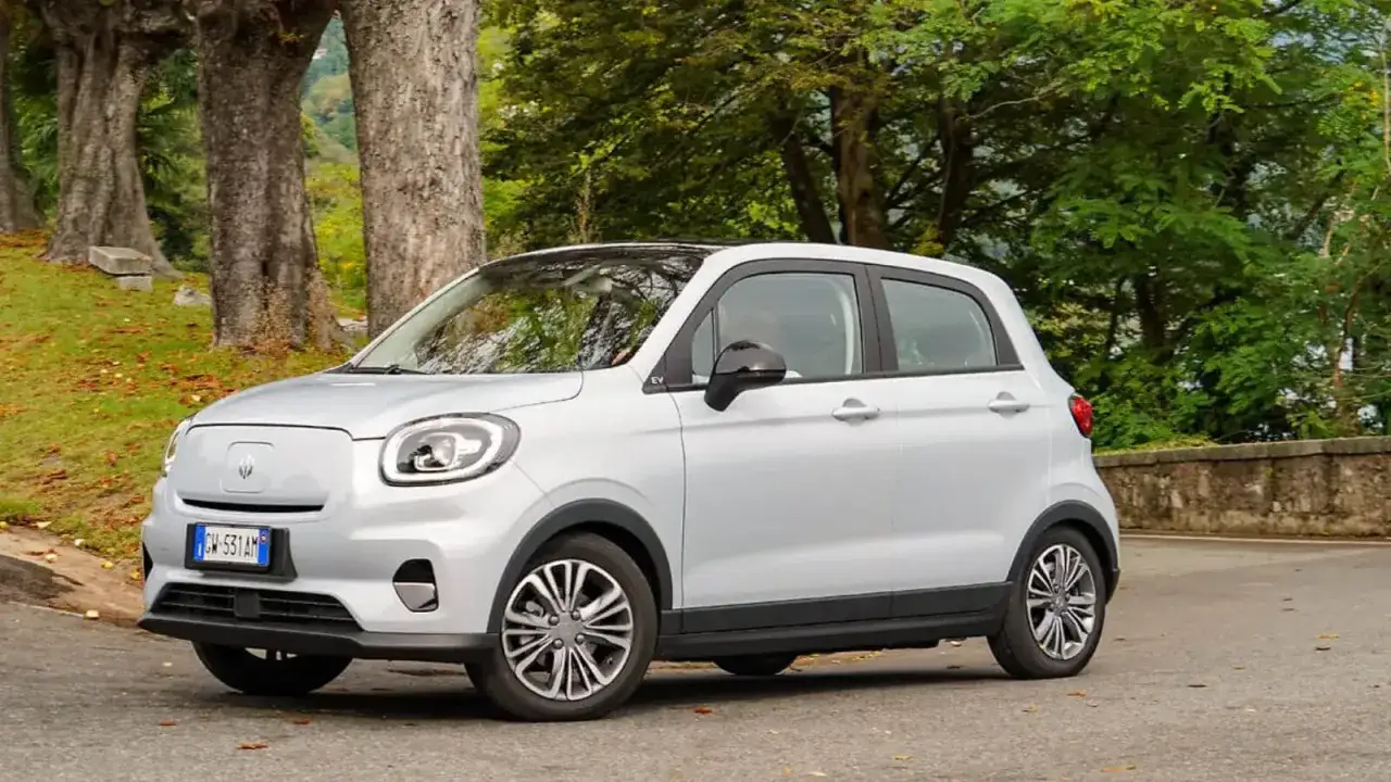 Srebrny, miejski samochód elektryczny na tle drzew. Zastanawiasz się, ile kosztuje najtańszy samochód elektryczny?