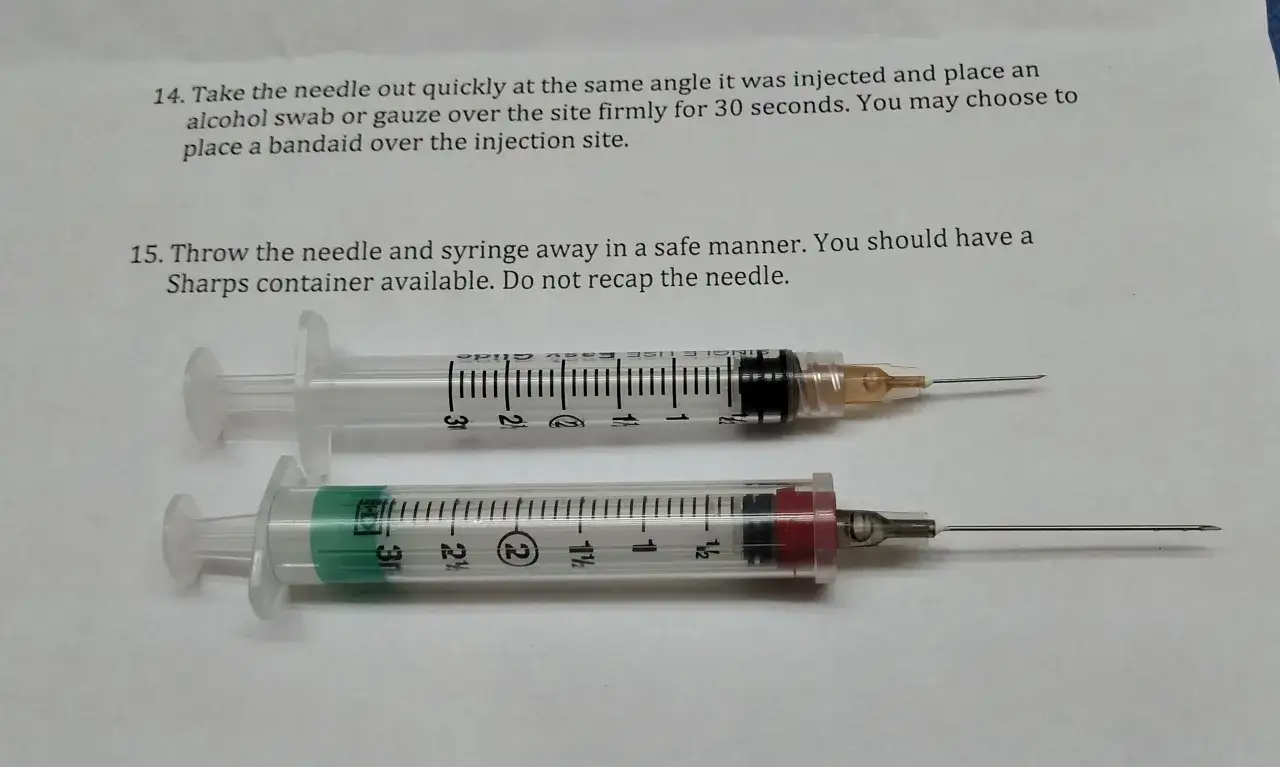 Dwie strzykawki z igłami, jedna z pomarańczową osłonką, druga z czerwoną. Pokazują, jaka igła do zastrzyku domięśniowego.