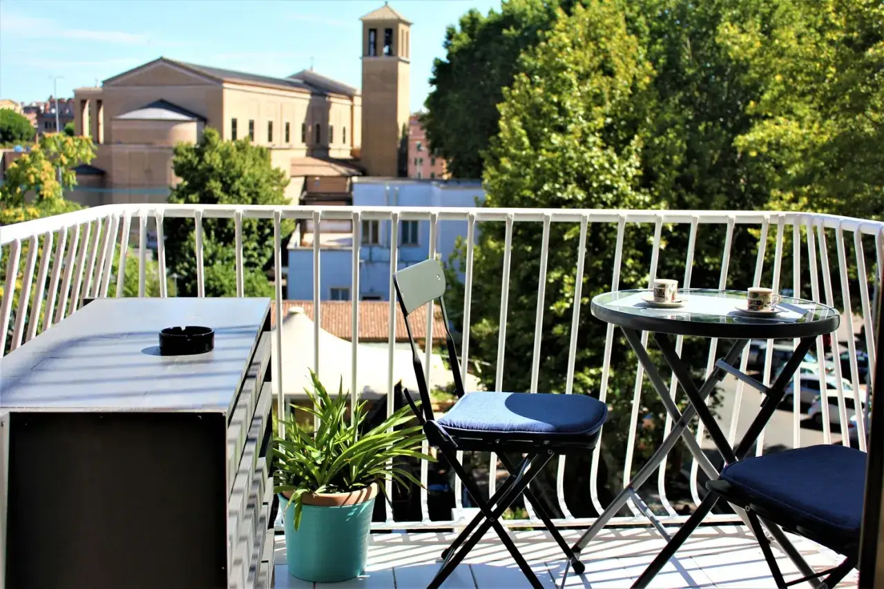 Balkon z widokiem na rzymskie budynki i zieleń, stolik z kawą.