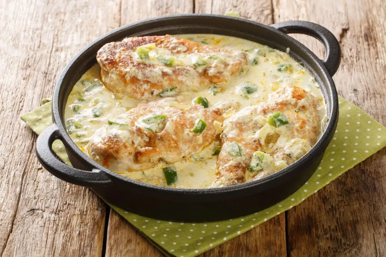 Pyszne piersi kurczaka w kremowym sosie z zieloną papryką. Idealne co na obiad z piersi z kurczaka, podane w żeliwnej patelni na drewnianym stole.