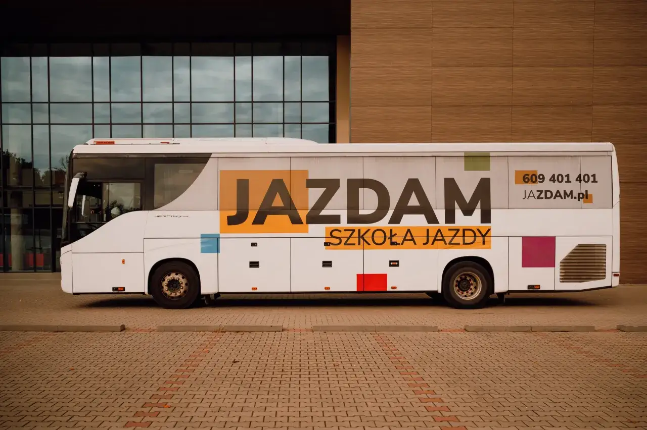 Biały autobus szkolny z napisem "JAZDAM SZKOŁA JAZDY" i numerem telefonu.
