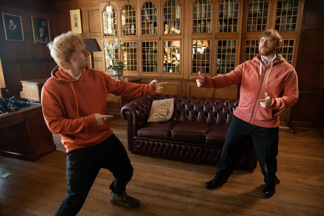 Dwóch Edów Sheeranów w pomarańczowych bluzach, jakby dyskutowali, czy Ed Sheeran grał w Harrym Potterze.