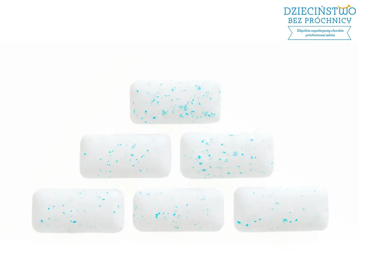 Białe gumy do żucia z niebieskimi drobinkami ułożone w piramidę. Żucie gumy pomaga zapobiegać próchnicy.