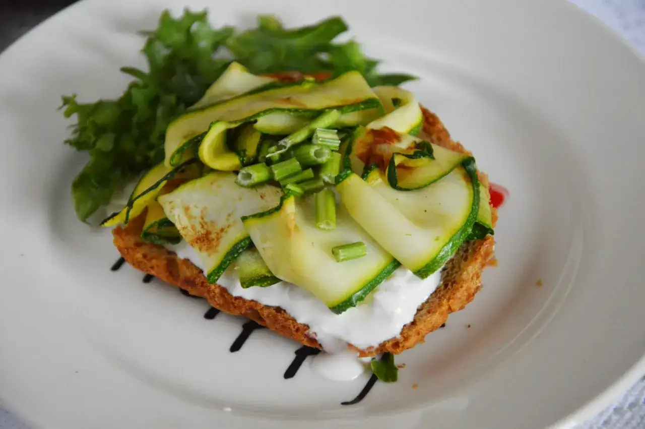 Kanapka z cukinią, serem i sałatą na białym talerzu.
