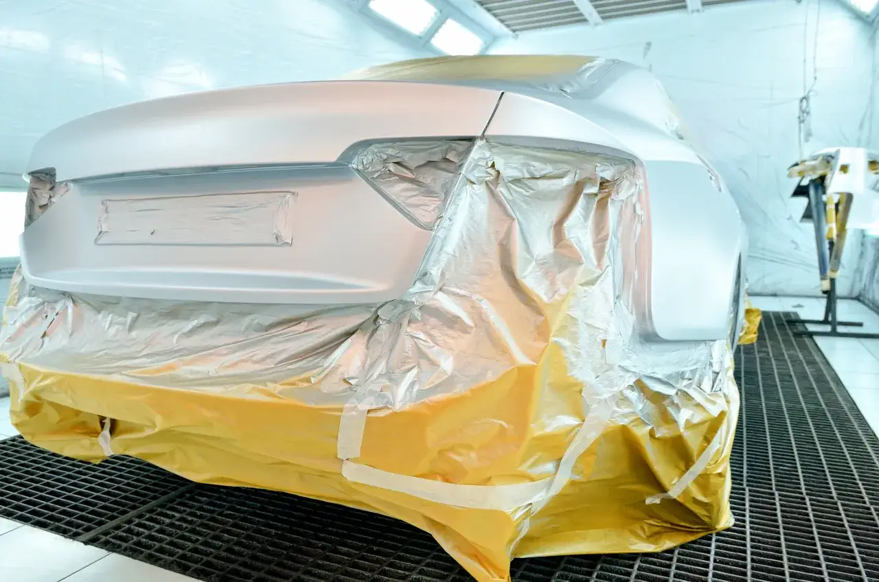 Samochód w kabinie lakierniczej, częściowo zakryty folią ochronną.