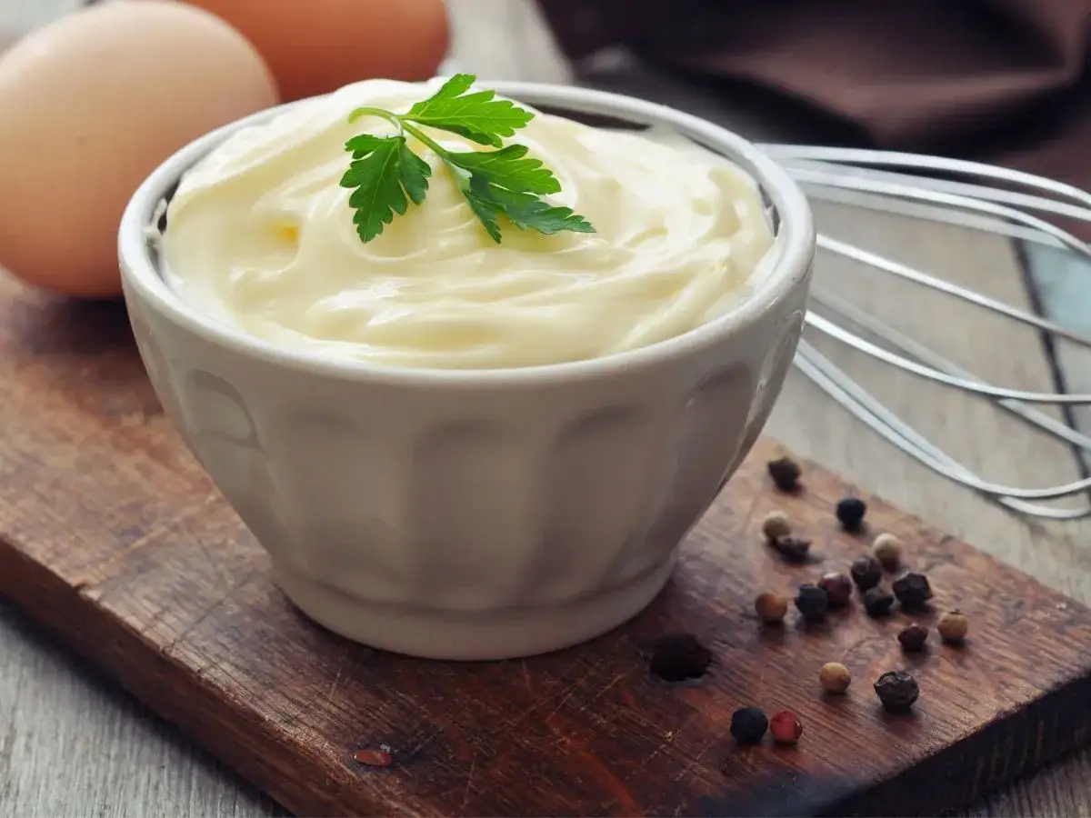 Aksamitny majonez domowy w miseczce, obok jajka, pieprz i trzepaczka. Idealny do sałatek!