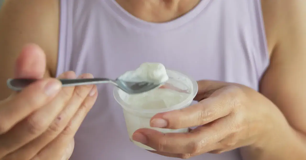 Kobieta trzymająca łyżkę z jogurtem i kubeczek jogurtu.