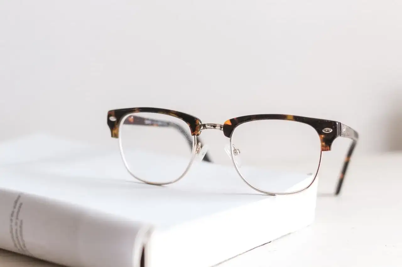 Okulary w stylu retro leżą na białej książce. Zastanawiasz się, od ilu dioptrii trzeba nosić okulary?