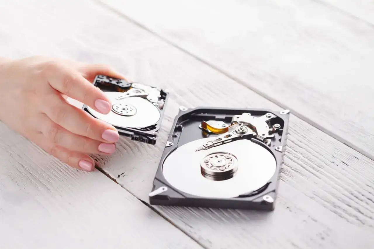Dłoń trzyma rozkręcony dysk twardy, obok leży drugi. Może to być przygotowanie do użycia programu do naprawy dysku.