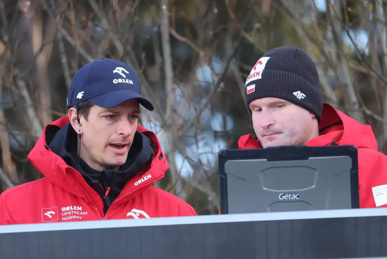 Dwóch trenerów w czerwonych kurtkach Orlen analizuje dane na tablecie. To oni decydują, kto trenuje polskich skoczków.