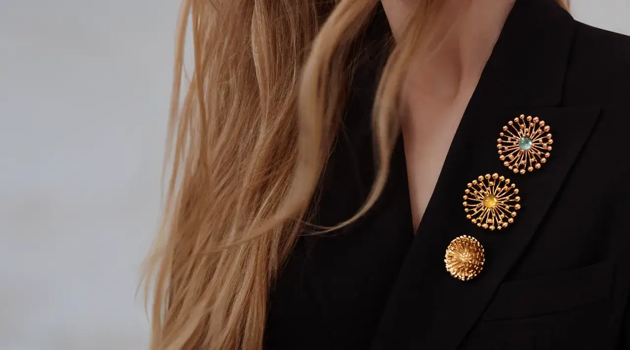 Elegancko jak nosić broszki: trzy złote ozdoby w kształcie kwiatów na czarnym blazerze.