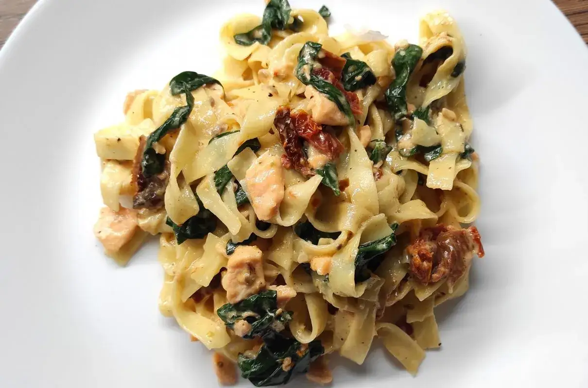 Pyszny makaron z łososiem i suszonymi pomidorami, podany na białym talerzu.