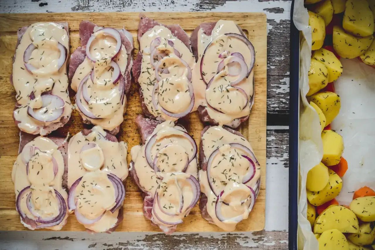 Plastry schabu w sosie z cebulą na desce, obok pieczone ziemniaki.