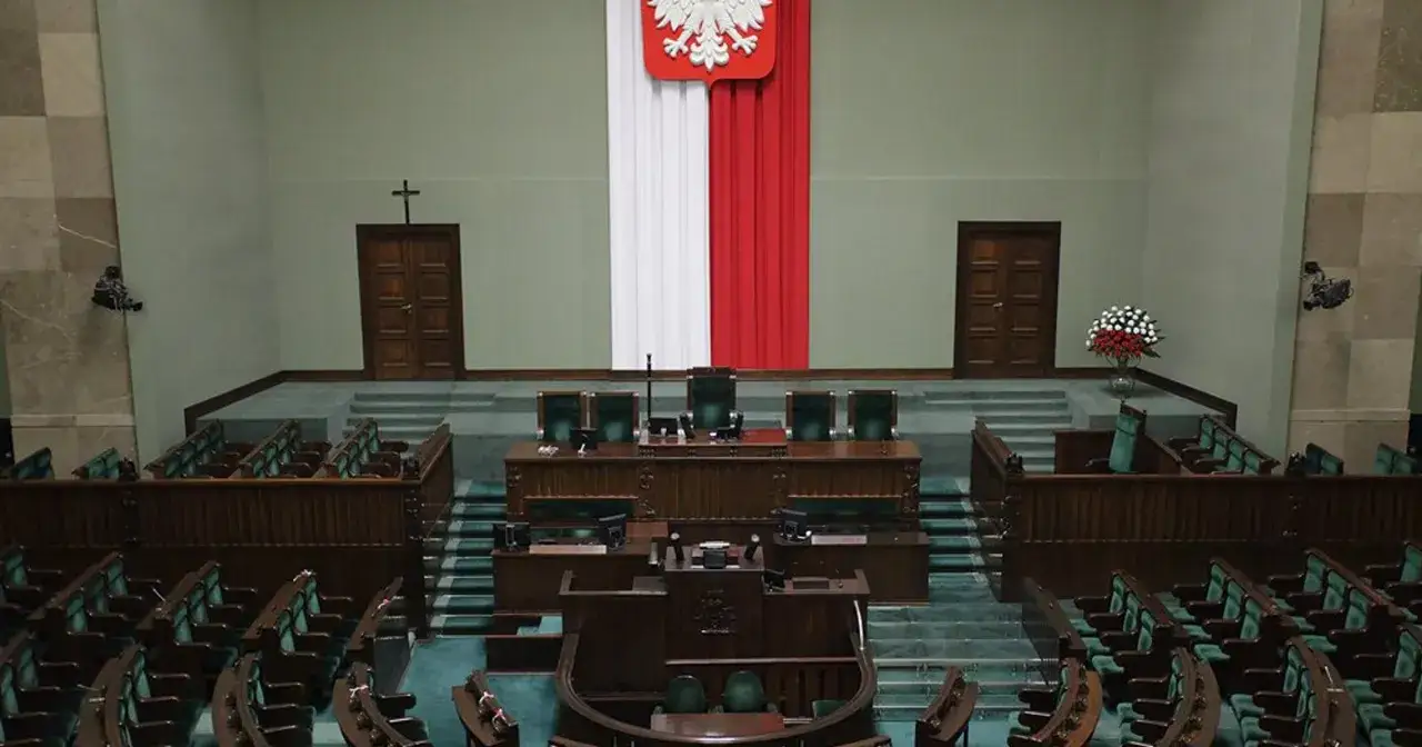 Pusta sala sejmowa z rzędami zielonych foteli i mównicą. Biało-czerwona flaga i godło Polski. Zastanawiasz się, ile jest posłów w sejmie?