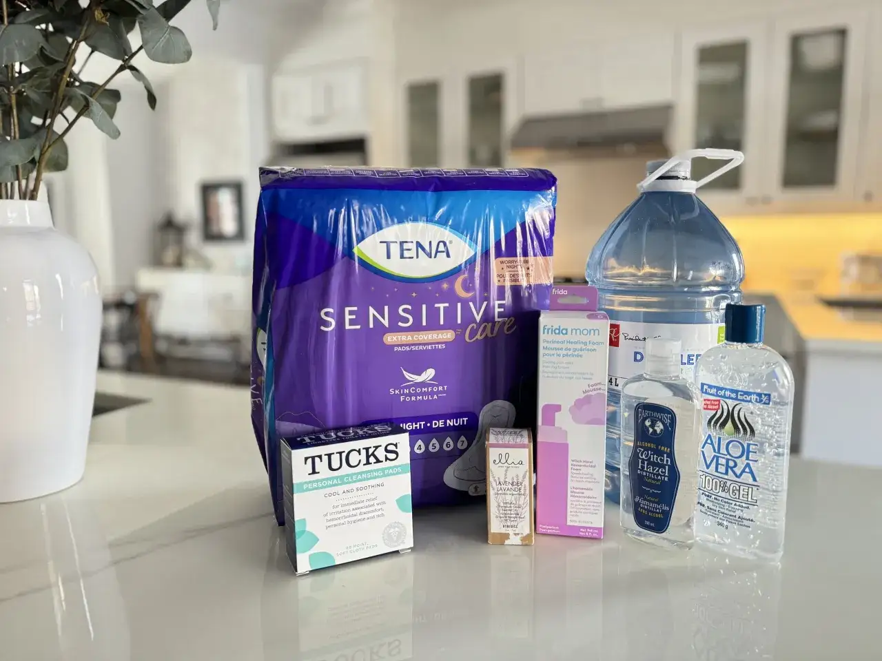 Zestaw produktów poporodowych: podpaski Tena, chusteczki Tucks, pianka do gojenia krocza Frida Mom, woda oczarowa i żel aloesowy.