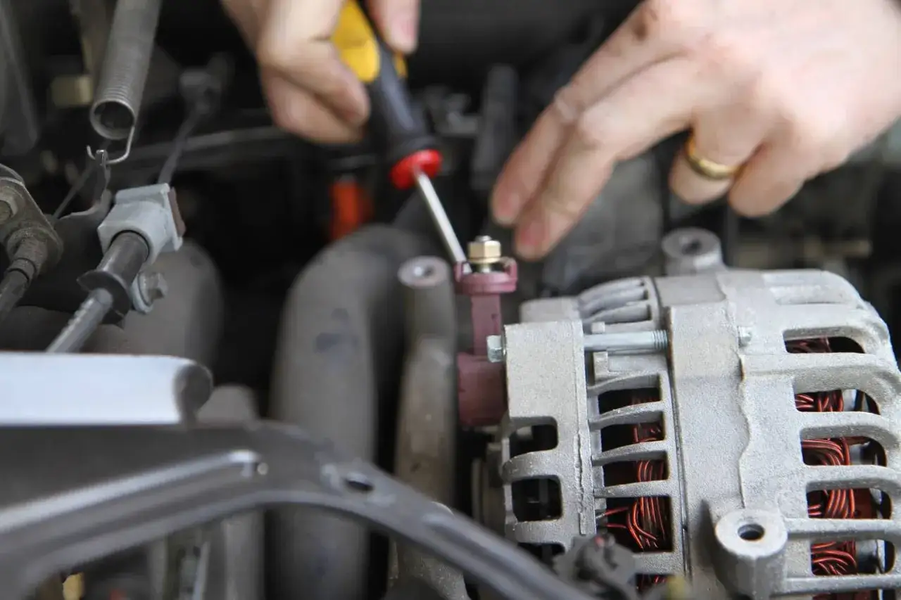 Mechanik dokręca śrubę przy alternatorze. Czas pracy: ile trwa wymiana alternatora w samochodzie?