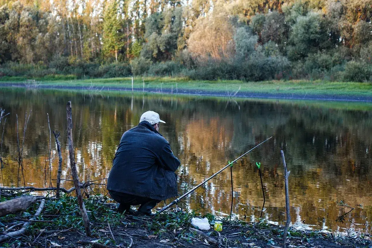 Wędkarz siedzi nad jeziorem, czekając na branie. Na brzegu leży zanęta na tołpyge, gotowa do użycia.