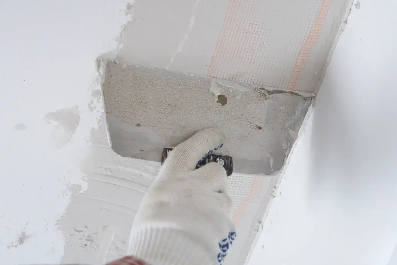 Ręka w rękawicy nakłada zaprawę na styropian przy suficie. Proces pokazujący, jak przykleić styropian do sufitu.